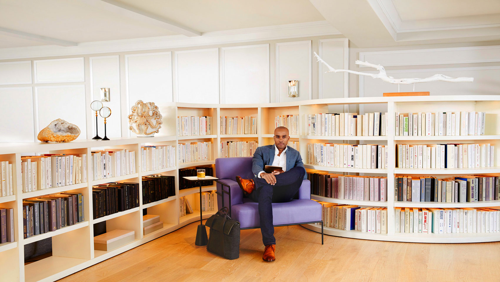 Man in business attire on accent chair surrounded by book-filled shelves