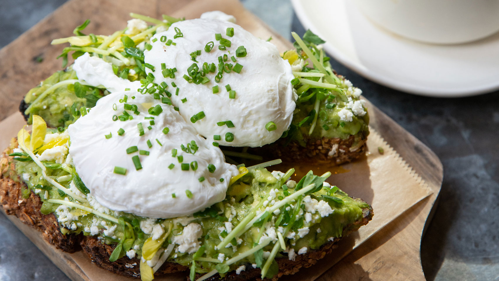 Avocado toast served on wooden slab next to plates