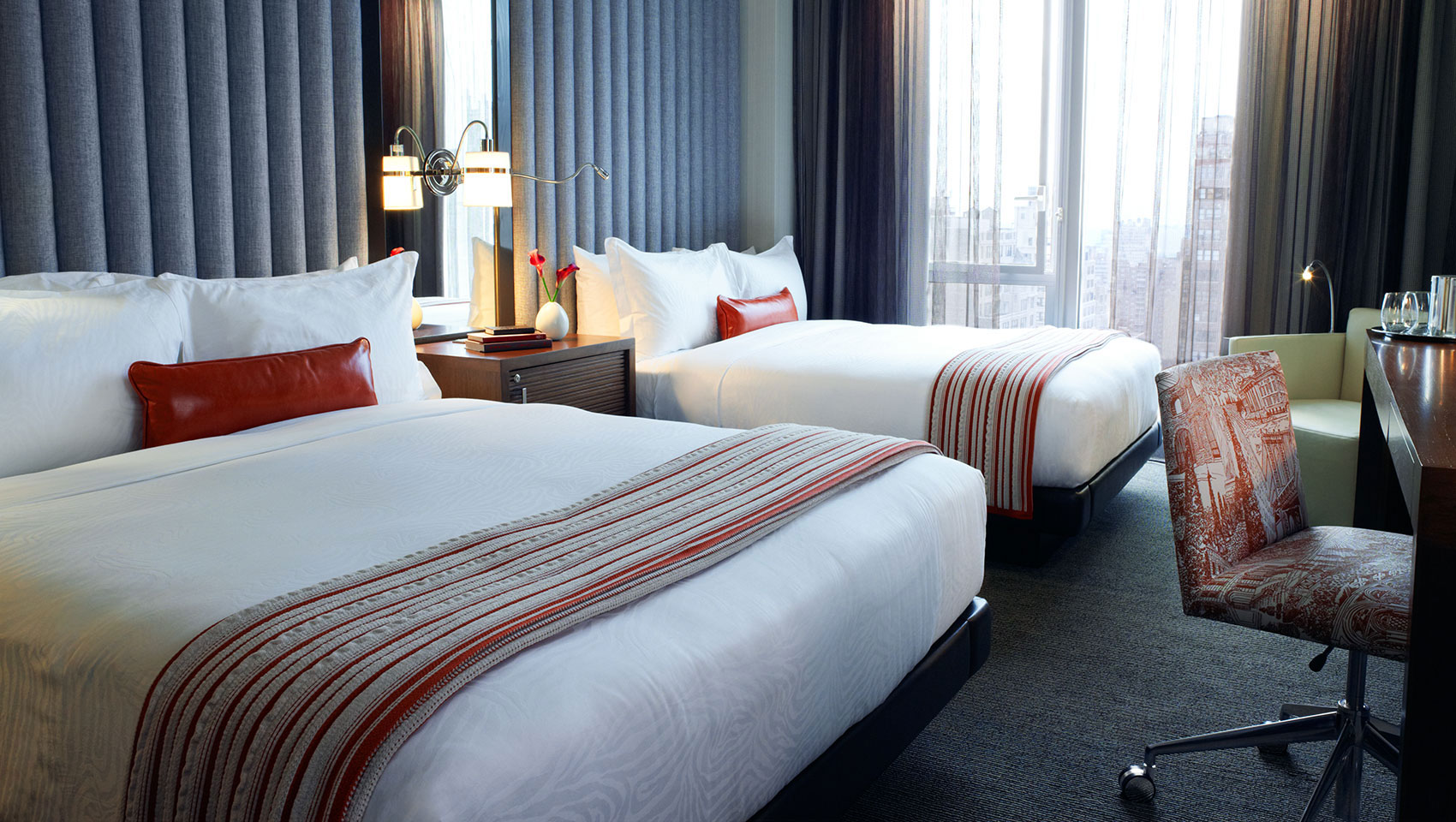 Two side-by-side queen beds next to large sunlit window