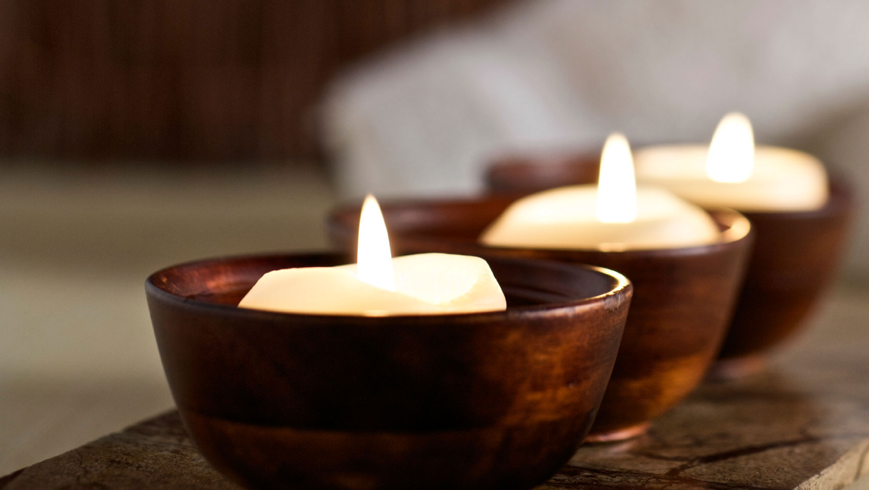 Close up view of 3 lit candles in wooden candle holders