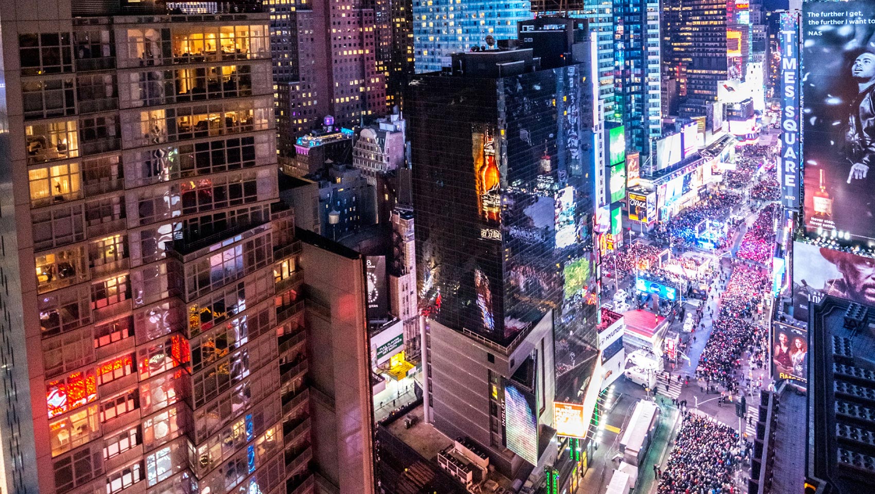 Times Square during nighttime with large crowds in the streets between tall buildings