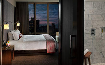 Kimpton Hotel Eventi guest room next to large window overlooking city buildings