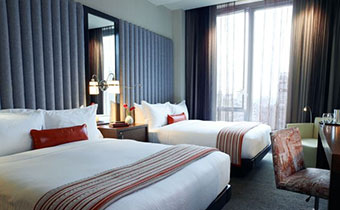 Two side-by-side queen beds next to large sunlit window